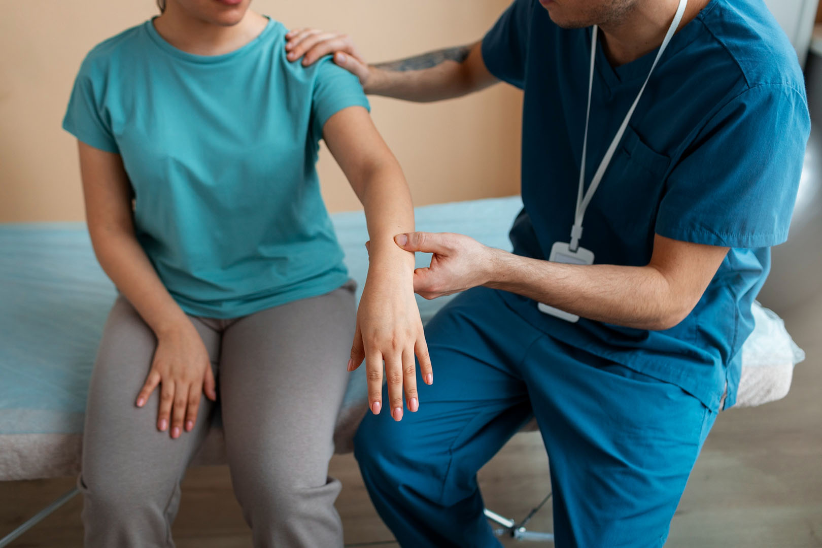 La fotografía muestra a un paciente jóven con hemiparesia, siendo tratado por un kinesiólogo, quien está apoyando para que estire su brazo con debilidad muscular